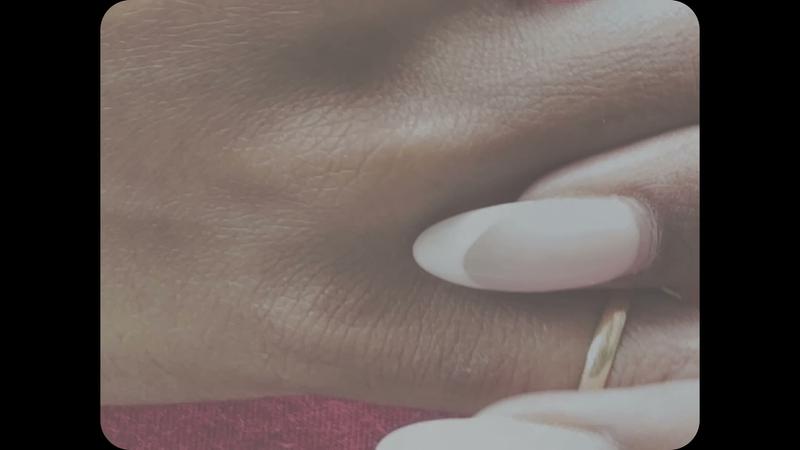 Fog of Meaning — film still: a hand with a gold ring resting on a warm maroon ground, in the film's soft retro frame